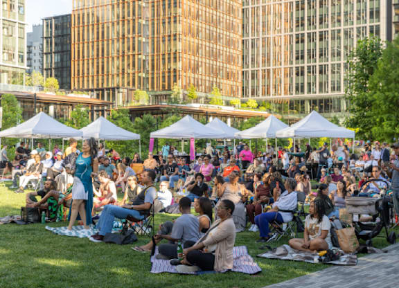 A large group of people are sitting on the grass in a park.