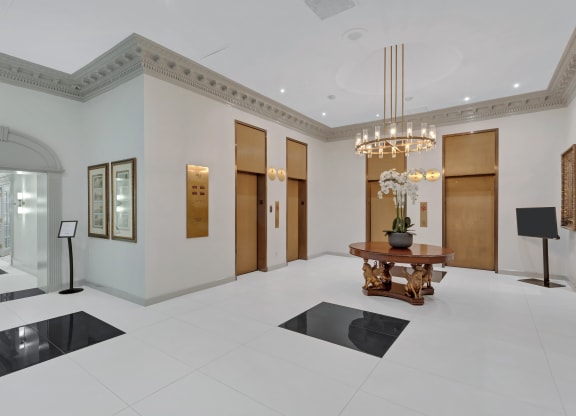 a lobby with a table and three elevators and a chandelier