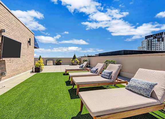 A sunny rooftop patio with a row of lounge chairs and a flat screen TV.
