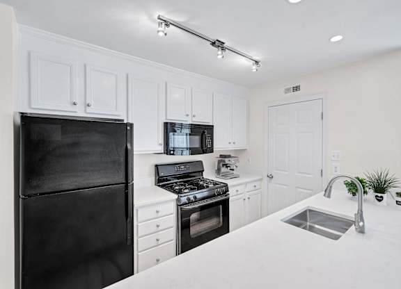 A black refrigerator is on the left in a white kitchen.