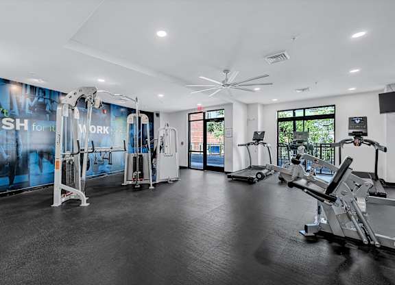 A gym with a variety of equipment including treadmills, weights, and a fan.