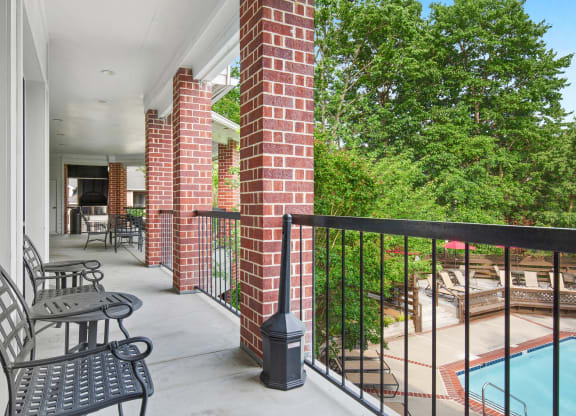 a balcony with two chairs and a table and a pool in the background