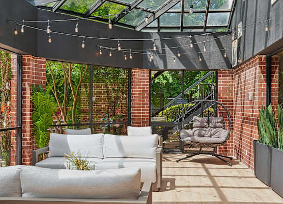 A patio with a white couch and a chair under a glass roof.