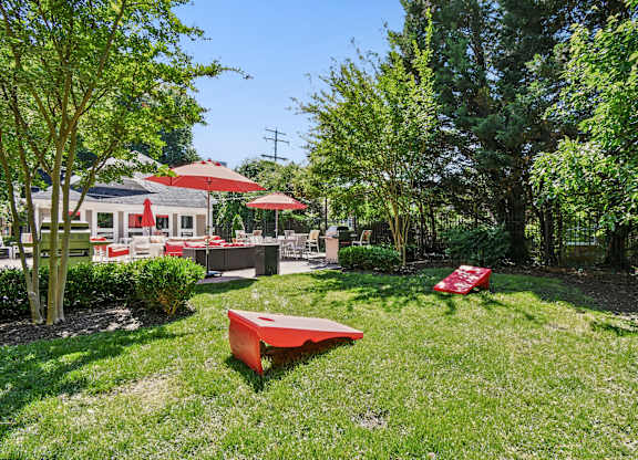 A red bench sits in a grassy area with trees and a building in the background.