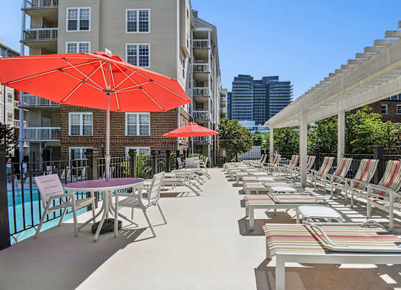 A patio with chairs and umbrellas is surrounded by buildings.