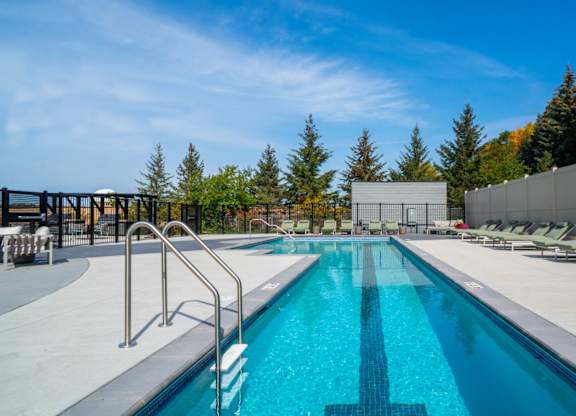 A large outdoor swimming pool surrounded by lounge chairs and trees.