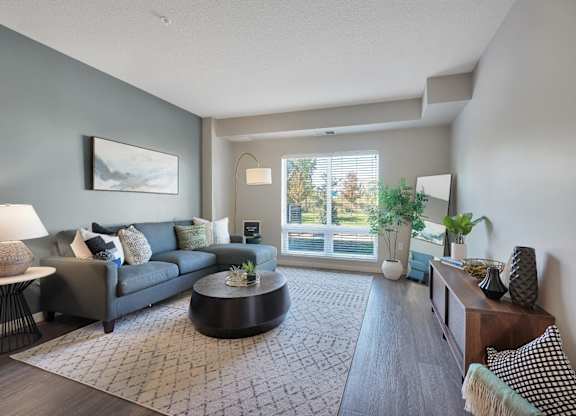 A living room with a grey couch, a coffee table, and a large window.