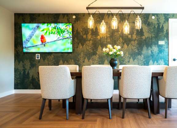 A dining room with a television mounted on the wall and a vase of flowers on the table.