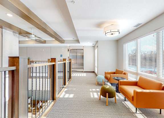 A long hallway with orange chairs and tables on the right side.