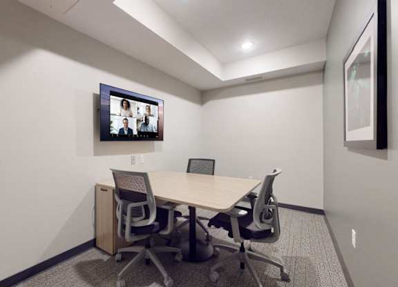 A conference room with a table, chairs and a screen on the wall.
