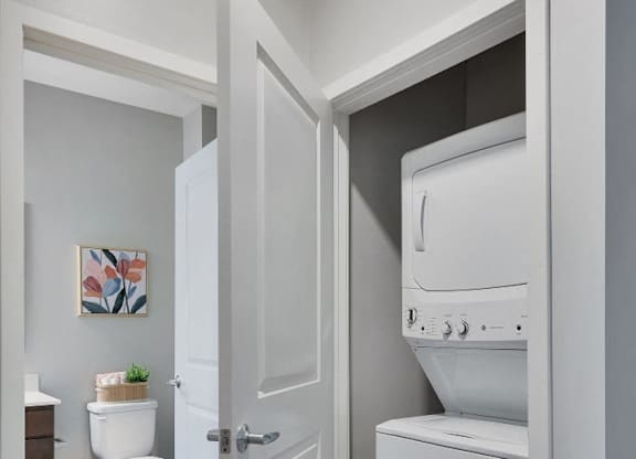 A white door opens to a bathroom with a toilet and a washing machine.