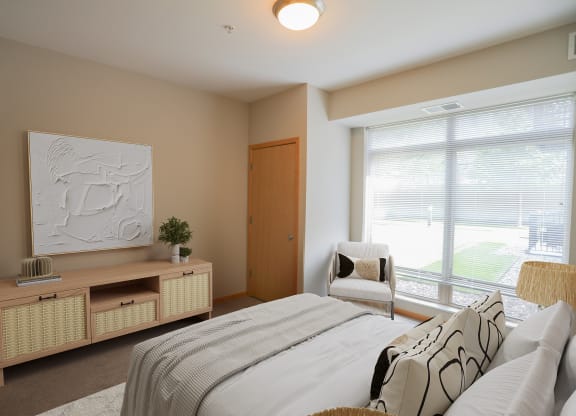 a bedroom with a large window and a bed with a white comforter