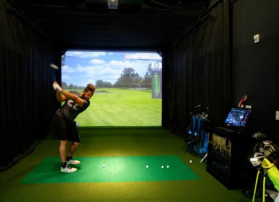 A man is playing golf indoors on a green mat.