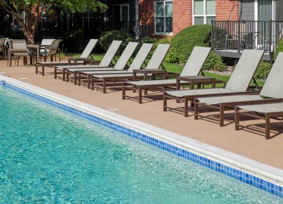 A pool with chairs and a building in the background.