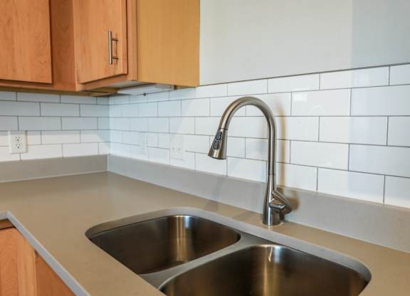 A kitchen sink with a chrome faucet and a white tile backsplash.