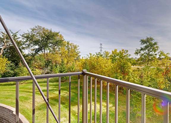 A balcony with a metal railing overlooks a green lawn and trees.