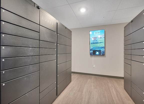 A hallway with a row of lockers on the left and a TV screen on the right.