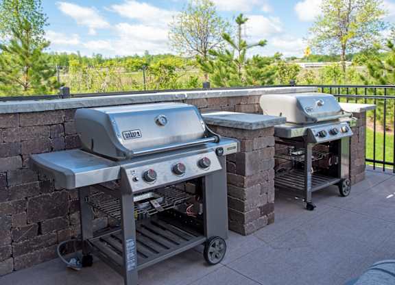 Two grills on a patio with a brick wall.