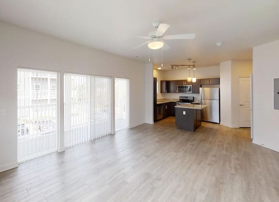 an empty living room with a kitchen and a ceiling fan