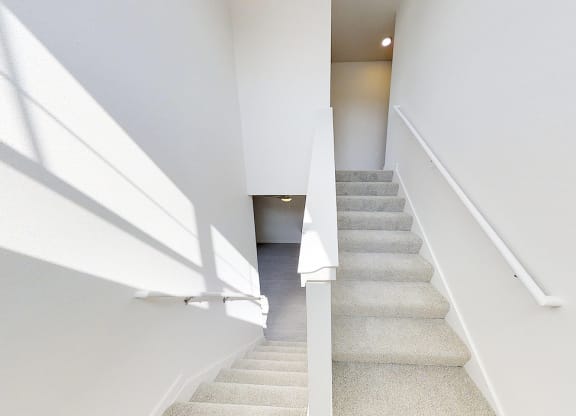 a view down the stairs of a hallway with white walls and a white stair rail
