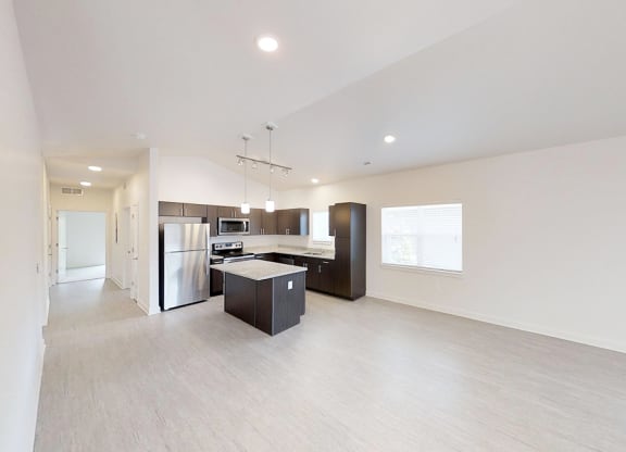 an empty living room and kitchen with a refrigerator and a sink