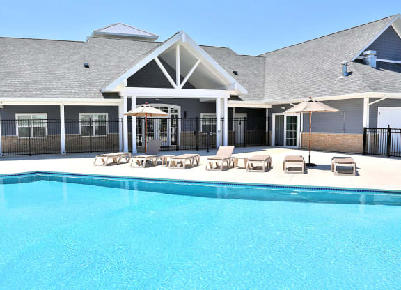 a large swimming pool in front of a building with chairs and umbrellas