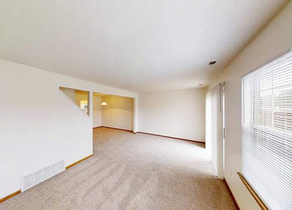 A spacious room with a carpeted floor and a window with blinds.