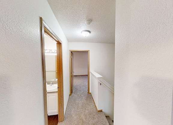 A hallway with a door on the left and a carpeted floor.