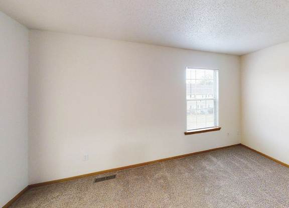 A room with a window and a carpeted floor.