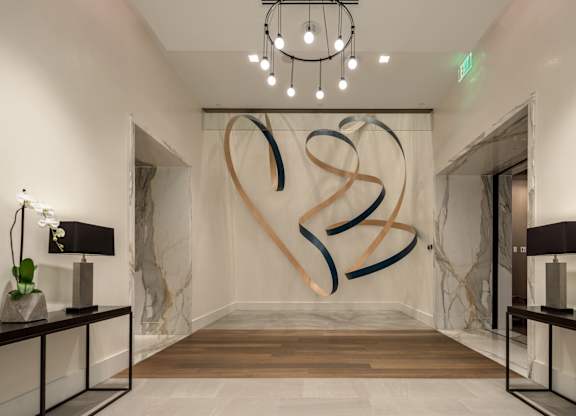 A hallway with a large artwork on the wall and two potted plants on either side.