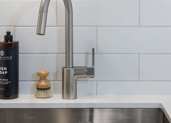 A modern kitchen sink with a chrome faucet and a bottle of soap.