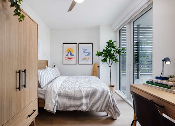 A bedroom with a bed, desk, and two framed pictures on the wall.