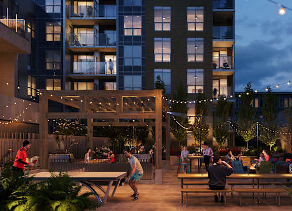 A group of people are sitting and standing on a patio with a building in the background.