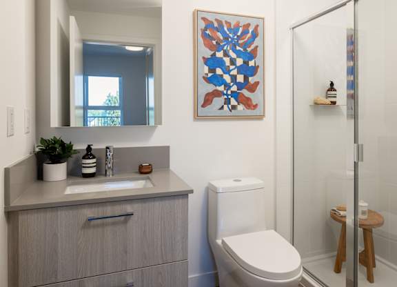 A bathroom with a toilet, sink, mirror, and a picture on the wall.