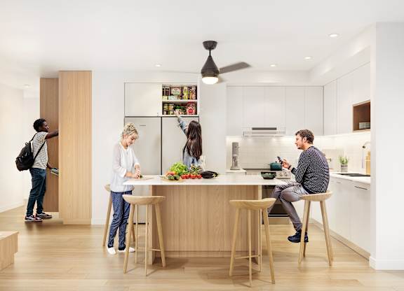 A man is sitting at a table in a kitchen with two women standing behind him.
