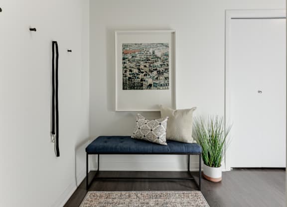 A picture frame with a picture of a cityscape is hanging on the wall above a bench with a cushion and two pillows.