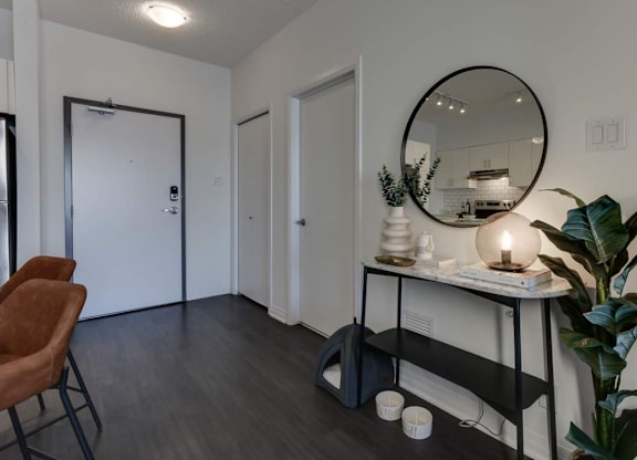 A room with a round mirror, a chair, a table with a vase and candle, and a plant.