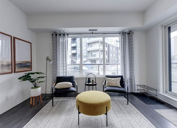 A living room with a yellow ottoman and two black chairs.