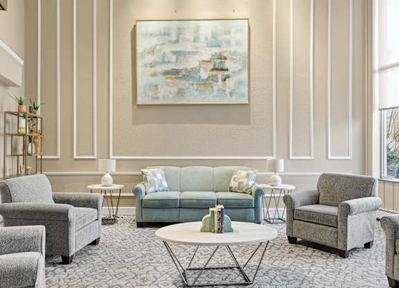 A living room with a grey couch, a green couch, and a painting on the wall.