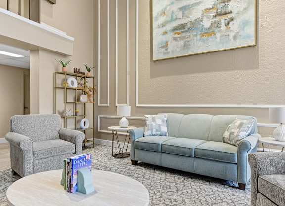 A living room with a grey couch, a grey armchair, a white coffee table, and a large abstract painting on the wall.