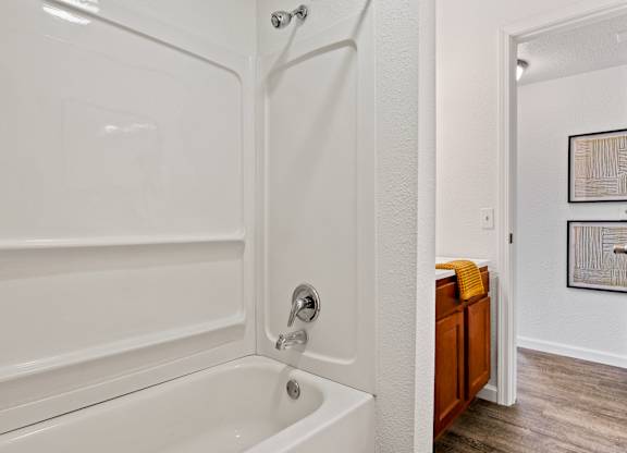 A white bathtub with a shower head and a wooden cabinet. at Vivo Toledo Apartments, Toledo, 43607