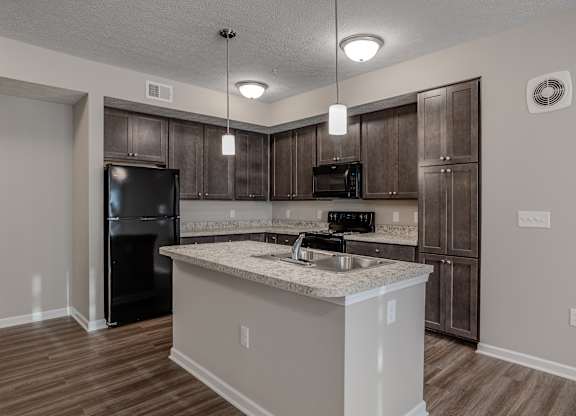 A kitchen with a black fridge, microwave, and oven, and a white island with a sink.at The Residences at Akita Lane, Canal Winchester, 43110
