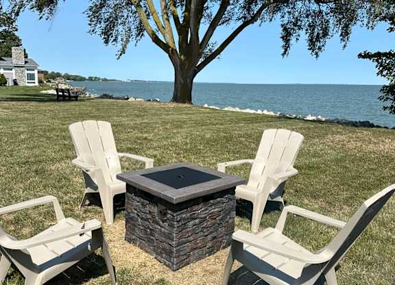 A fire pit surrounded by three chairs on a lawn.