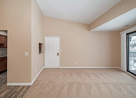 A room with a white door and a window with a view of a balcony.