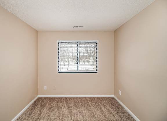 A bedroom with a window and carpeted floor.