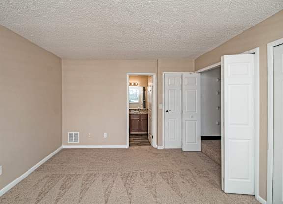 A room with beige walls and carpeting, with a doorway leading to another room.