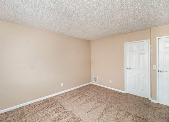 A room with beige walls and carpeted floor with two white doors.
