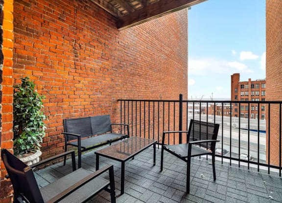 A balcony with a black metal railing and furniture including a couch, chair and table.