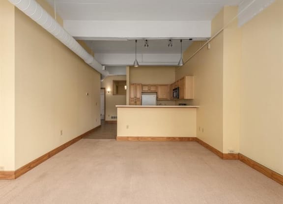 an empty living room with a kitchen in the background