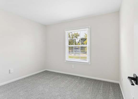 A room with a window and a grey carpet.
